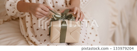 Caucasian child hands opening gift box on beige bed in cozy room 133979204