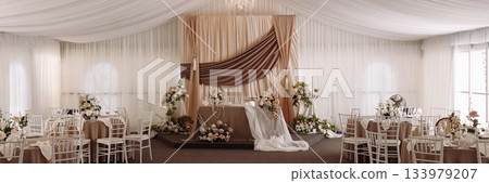 Banner wedding banquet hall with elegant stage and round tables decorated in beige Banner wedding banquet hall with elegant stage and round tables decorated in beige 133979207