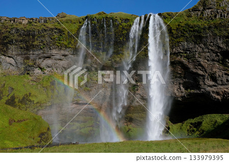 A waterfall flows down a cliff surrounded by lush green forest 133979395