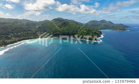 Curving coastline with green hills meeting the turquoise water, dotted with waves. Seychelles, Mahe. Curving coastline with green hills meeting the turquoise water, dotted with waves. Seychelles, Mahe. 133979466