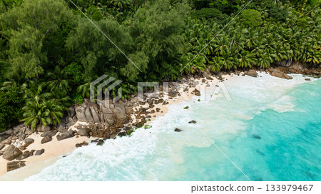 Tropical beach with clear turquoise ocean waters, large rocks, and lush greenery. Seychelles, Mahe. Anse Intendance. 133979467