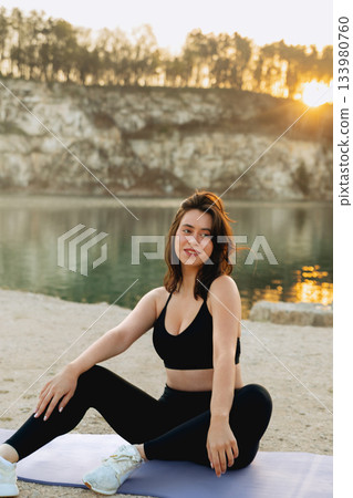 Woman practicing yoga at sunset by the lake in a serene outdoor setting surrounded by nature and mountains Woman practicing yoga at sunset by the lake in a serene outdoor setting surrounded by nature and mountains 133980760