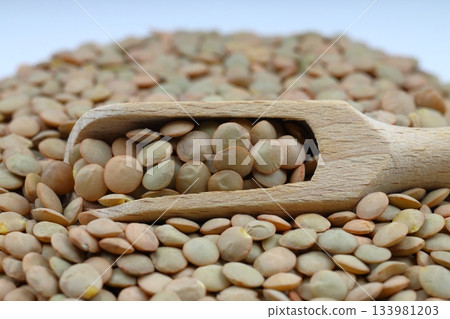 Green Lentils in a wooden spoon close-up on a wooden background. Vegetarian food. Green Lentils in a wooden spoon close-up on a wooden background. Vegetarian food. 133981203