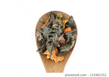 A pile of dry green tea on a white background. Apple flavor. Top view, isolated, close-up. Extreme close-up on the spoon. A pile of dry green tea on a white background. Apple flavor. Top view, isolated, close-up. Extreme close-up on the spoon. 133981352