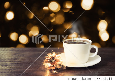 Hot coffee with steam in white cup on rustic wooden table, golden bokeh lights background. Christmas atmosphere, cozy evening winter concept. Hot coffee with steam in white cup on rustic wooden table, golden bokeh lights background. Christmas atmosphere, cozy evening winter concept. 133981711