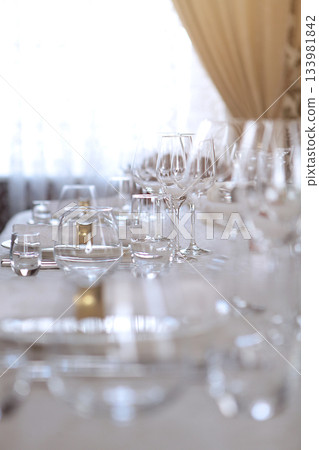 Festive table setting. The concept of the holiday. Wine glasses on the table. White plates. VIP lounge in the restaurant. A white tablecloth. Out of focus. Part of the interior. Festive table setting. The concept of the holiday. Wine glasses on the table. White plates. VIP lounge in the restaurant. A white tablecloth. Out of focus. Part of the interior. 133981842