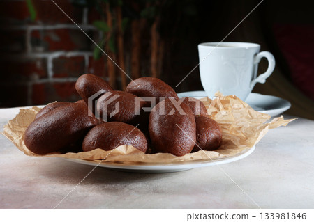 Chocolate brownie "Potato". A sweet dessert made from butter and cocoa. There is a white porcelain cup on the table. 133981846