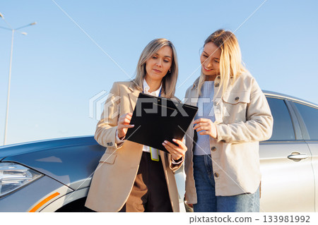 Female instructor explaining driving test details to learner driver near car Female instructor explaining driving test details to learner driver near car 133981992