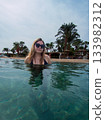 A young woman with sun glasses swimming in the blue sea. A blue hazy sky in the background 133982312