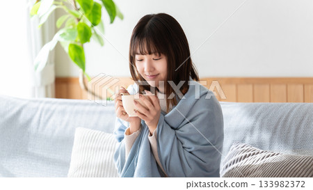A woman wearing a blanket and drinking a hot drink A woman wearing a blanket and drinking a hot drink 133982372