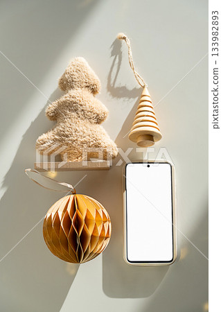 Smartphone with white screen next to Christmas ornament and Christmas tree decoration Smartphone with white screen next to Christmas ornament and Christmas tree decoration 133982893