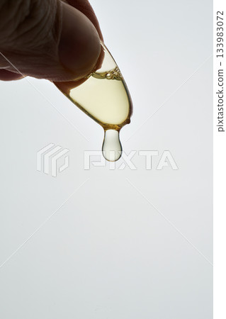 Hand squeezing omega 3 capsule releasing oil drop 133983072
