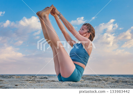 Woman practicing Ubhaya Padangusthasana on the beach during sunset Woman practicing Ubhaya Padangusthasana on the beach during sunset 133983442