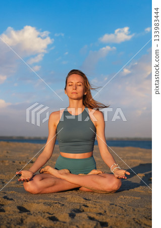 Woman practicing Padmasana yoga on a beach during a serene evening Woman practicing Padmasana yoga on a beach during a serene evening 133983444