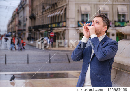Man plays harmonica outdoors in city street 133983468