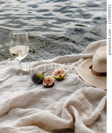 on the water, a beige linen blanket with a hat and a wine glass on top of it, halved figs next to them, evoking summer vibes on the water, a beige linen blanket with a hat and a wine glass on top of it, halved figs next to them, evoking summer vibes 133984052