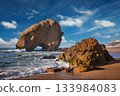 Penedo do Guincho rock at Praia da Santa Cruz as waves crash against the sandy shore during a colorful sunset. 133984083