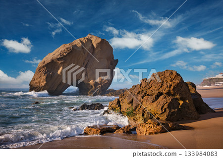 Penedo do Guincho rock at Praia da Santa Cruz as waves crash against the sandy shore during a colorful sunset. Penedo do Guincho rock at Praia da Santa Cruz as waves crash against the sandy shore during a colorful sunset. 133984083