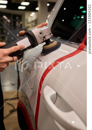 Polishing black car surface thoroughly, Detailed buffing to achieve showroom quality shine, Expert technician uses orbital buffer and foam pad to enhance vehicle gloss 133984101
