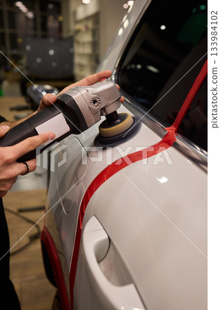 Polishing black car surface thoroughly, Detailed buffing to achieve showroom quality shine, Expert technician uses orbital buffer and foam pad to enhance vehicle gloss Polishing black car surface thoroughly, Detailed buffing to achieve showroom quality shine, Expert technician uses orbital buffer and foam pad to enhance vehicle gloss 133984102