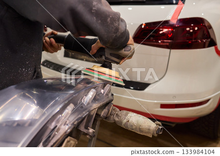 Hands refining car lamps professionally, Orbital buffer restoring clarity to headlights, Closeup of technician smoothing car headlight with orbital buffer and polishing tools 133984104
