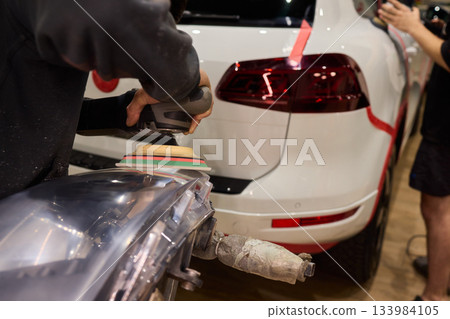 Hands refining car lamps professionally, Orbital buffer restoring clarity to headlights, Closeup of technician smoothing car headlight with orbital buffer and polishing tools 133984105