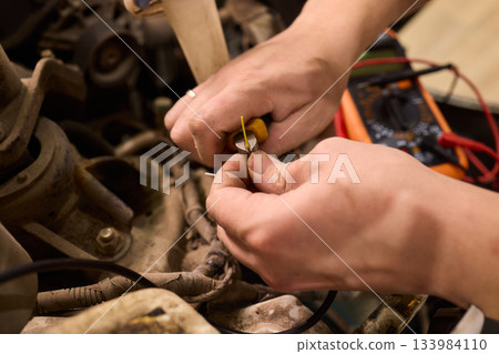 Electrical diagnostics performed on car wiring with multimeter tools, Technician connecting and repairing vehicle wiring under warm workshop lighting conditions 133984110