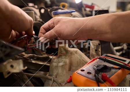 Mechanic accurately measures vehicle wiring with specialized tools, Skilled technician conducts detailed electrical checks on car wiring in workshop environment Mechanic accurately measures vehicle wiring with specialized tools, Skilled technician conducts detailed electrical checks on car wiring in workshop environment 133984111