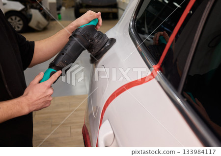 Polishing black car surface thoroughly, Detailed buffing to achieve showroom quality shine, Expert technician uses orbital buffer and foam pad to enhance vehicle gloss 133984117