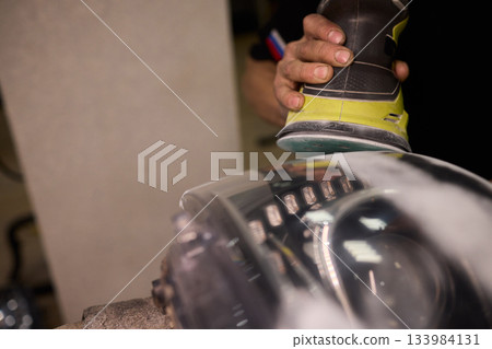 Hands refining car lamps professionally, Orbital buffer restoring clarity to headlights, Closeup of technician smoothing car headlight with orbital buffer and polishing tools Hands refining car lamps professionally, Orbital buffer restoring clarity to headlights, Closeup of technician smoothing car headlight with orbital buffer and polishing tools 133984131