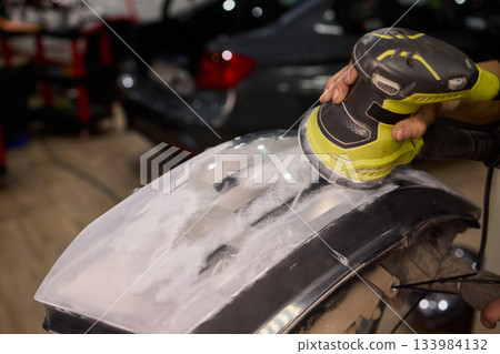 Hands refining car lamps professionally, Orbital buffer restoring clarity to headlights, Closeup of technician smoothing car headlight with orbital buffer and polishing tools Hands refining car lamps professionally, Orbital buffer restoring clarity to headlights, Closeup of technician smoothing car headlight with orbital buffer and polishing tools 133984132