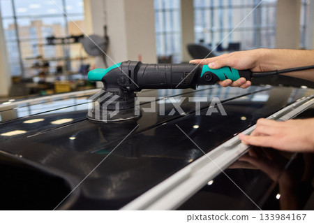 Polishing black car surface thoroughly, Detailed buffing to achieve showroom quality shine, Expert technician uses orbital buffer and foam pad to enhance vehicle gloss 133984167