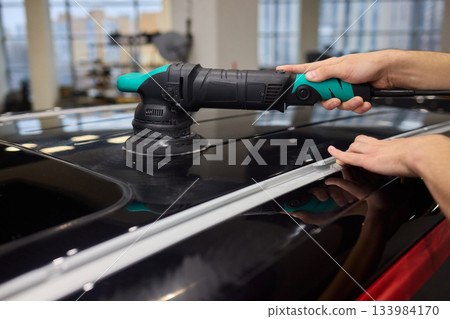 Polishing black car surface thoroughly, Detailed buffing to achieve showroom quality shine, Expert technician uses orbital buffer and foam pad to enhance vehicle gloss Polishing black car surface thoroughly, Detailed buffing to achieve showroom quality shine, Expert technician uses orbital buffer and foam pad to enhance vehicle gloss 133984170