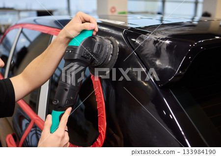 Polishing black car surface thoroughly, Detailed buffing to achieve showroom quality shine, Expert technician uses orbital buffer and foam pad to enhance vehicle gloss Polishing black car surface thoroughly, Detailed buffing to achieve showroom quality shine, Expert technician uses orbital buffer and foam pad to enhance vehicle gloss 133984190