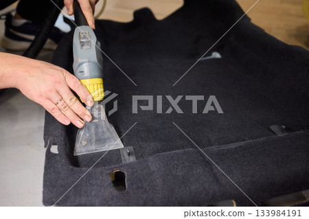 Automotive cleaning process, Professional vehicle upholstery maintenance and dirt removal, Detailed view of cleaning device removing grime from dark fabric upholstery 133984191
