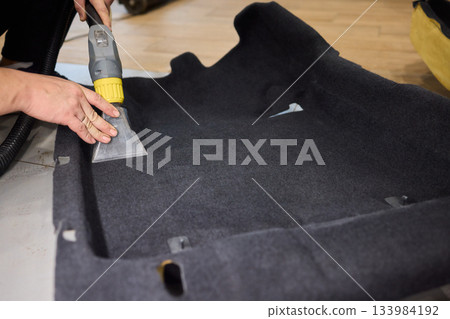 Automotive cleaning process, Professional vehicle upholstery maintenance and dirt removal, Detailed view of cleaning device removing grime from dark fabric upholstery 133984192