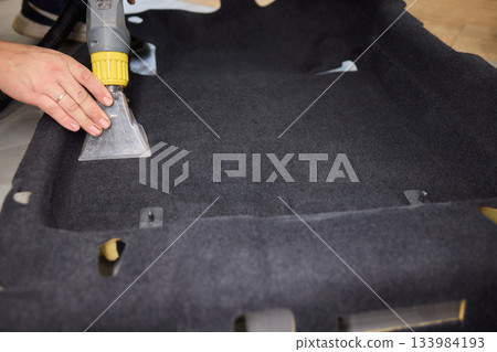 Automotive cleaning process, Professional vehicle upholstery maintenance and dirt removal, Detailed view of cleaning device removing grime from dark fabric upholstery 133984193
