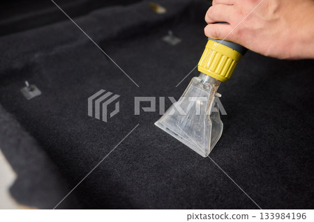 Automotive cleaning process, Professional vehicle upholstery maintenance and dirt removal, Detailed view of cleaning device removing grime from dark fabric upholstery 133984196