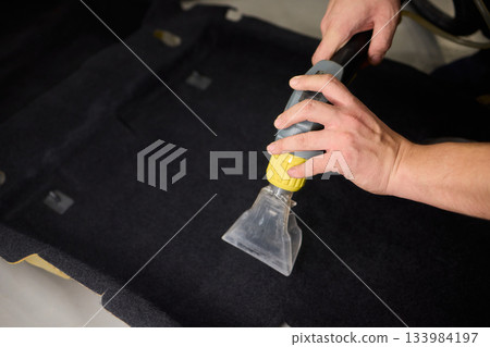 Automotive cleaning process, Professional vehicle upholstery maintenance and dirt removal, Detailed view of cleaning device removing grime from dark fabric upholstery Automotive cleaning process, Professional vehicle upholstery maintenance and dirt removal, Detailed view of cleaning device removing grime from dark fabric upholstery 133984197