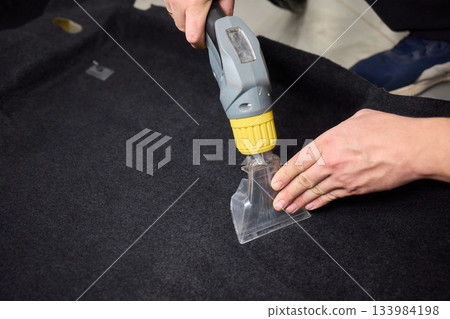 Automotive cleaning process, Professional vehicle upholstery maintenance and dirt removal, Detailed view of cleaning device removing grime from dark fabric upholstery 133984198