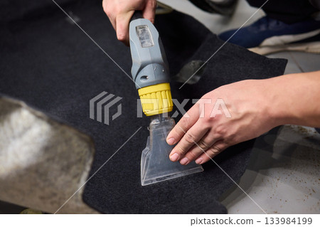 Automotive cleaning process, Professional vehicle upholstery maintenance and dirt removal, Detailed view of cleaning device removing grime from dark fabric upholstery 133984199