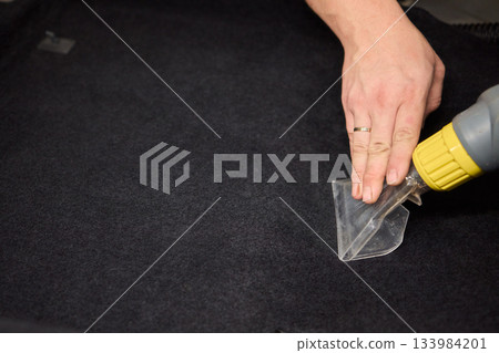 Automotive cleaning process, Professional vehicle upholstery maintenance and dirt removal, Detailed view of cleaning device removing grime from dark fabric upholstery 133984201