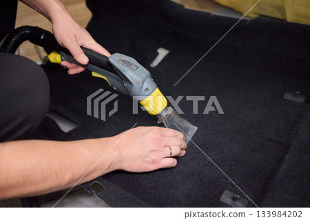 Automotive cleaning process, Professional vehicle upholstery maintenance and dirt removal, Detailed view of cleaning device removing grime from dark fabric upholstery Automotive cleaning process, Professional vehicle upholstery maintenance and dirt removal, Detailed view of cleaning device removing grime from dark fabric upholstery 133984202