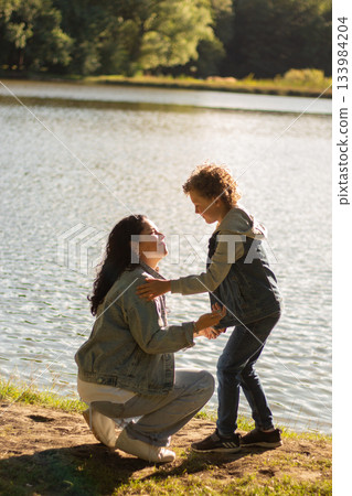 Peaceful moment of mother and son sit on grass, engaged in deep conversation. Natural setting and their focused interaction highlight connection and quality time. Family concept. High quality image. Peaceful moment of mother and son sit on grass, engaged in deep conversation. Natural setting and their focused interaction highlight connection and quality time. Family concept. High quality image. 133984204