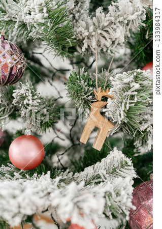 A young child placing decorations on a snowy Christmas tree near a bright window. The scene captures holiday warmth, family traditions, and a cozy seasonal mood A young child placing decorations on a snowy Christmas tree near a bright window. The scene captures holiday warmth, family traditions, and a cozy seasonal mood 133984317