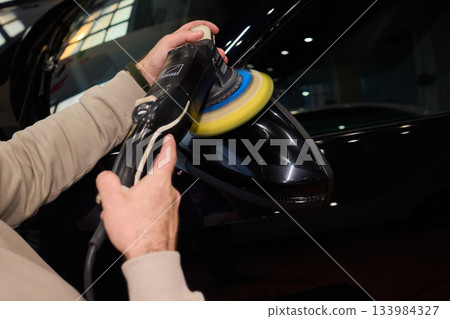 Polishing black car surface thoroughly, Detailed buffing to achieve showroom quality shine, Expert technician uses orbital buffer and foam pad to enhance vehicle gloss 133984327