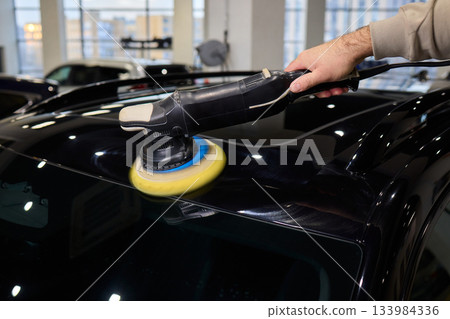 Polishing black car surface thoroughly, Detailed buffing to achieve showroom quality shine, Expert technician uses orbital buffer and foam pad to enhance vehicle gloss Polishing black car surface thoroughly, Detailed buffing to achieve showroom quality shine, Expert technician uses orbital buffer and foam pad to enhance vehicle gloss 133984336