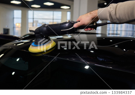Polishing black car surface thoroughly, Detailed buffing to achieve showroom quality shine, Expert technician uses orbital buffer and foam pad to enhance vehicle gloss 133984337