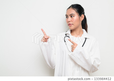 Woman Doctor with Stethoscope in White Uniform on Plain Background Pointing Finger Woman Doctor with Stethoscope in White Uniform on Plain Background Pointing Finger 133984412