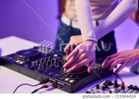 DJ setup overview, Energetic club DJ performing with digital controller in action, Content creator mixing music live using digital turntables under vibrant stage lights 133984424